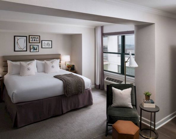 Double bed guest room in Claridge House, with art on the wall, window, and comfortable chair, footstool, and coffee table.