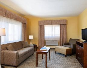 Guest room lounge in Holiday Inn Express Philadelphia Airport, with sofa, chair, TV, and foot stool.