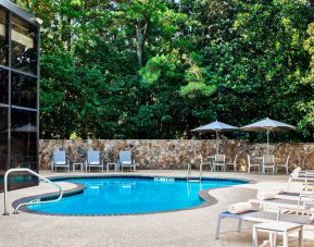 The hotel’s outdoor swimming pool has surrounding loungers and nearby trees.