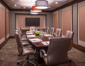 Hotel meeting room, featuring long wooden table and surrounding leather chairs.