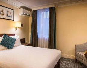 Double bed in a standard room at the Thistle London Heathrow Terminal 5, with nearby window and chair.