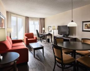 Guest room lounge in Les Suites Hotel Ottawa, with workspace desk and chair, plus sofa, chairs, and tables.