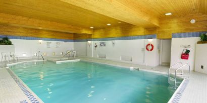 The hotel’s indoor pool is brightly lit and has chairs by the side.