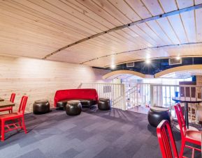 Second floor loft with arc planked ceiling, blue carpet, red chairs and small tables to work or socialize from.