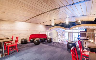 Second floor loft with arc planked ceiling, blue carpet, red chairs and small tables to work or socialize from.