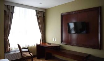 A Queens Hotel guest room with chair and table for working, and a nearby window.