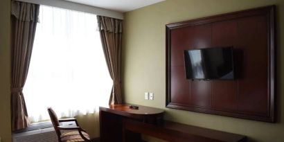 A Queens Hotel guest room with chair and table for working, and a nearby window.