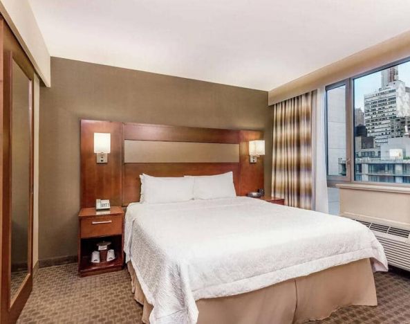 Double bed guest room in the Hampton Inn Manhattan Grand Central, NY, with large window offering a city view.