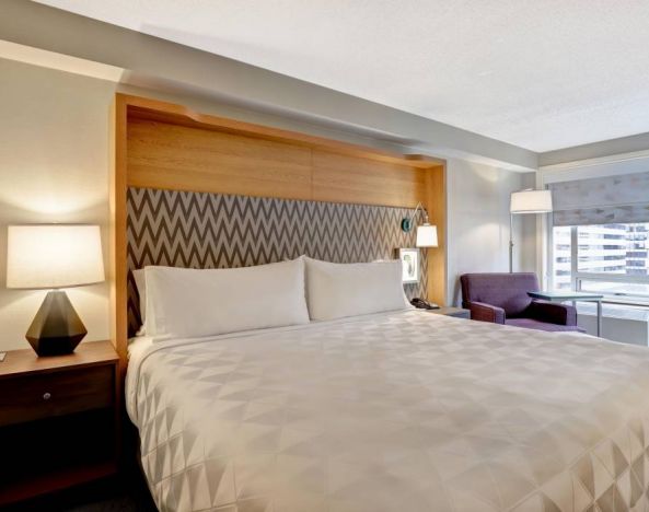 Double bed guest room in the Holiday Inn Ottawa Downtown Parliament Hill, with nearby chair and window.