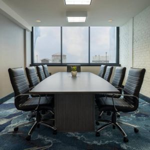 Hotel meeting room with a long wooden table and surrounding leather chairs.