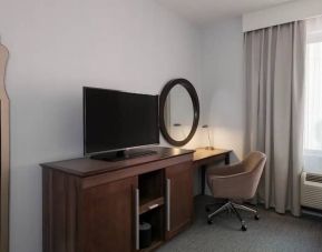 Wooden dark-stained television stand with TV, workspace to the right with desk lamp, phone, mirror directly ahead.