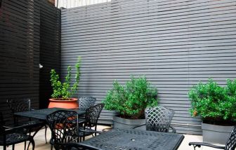 Patio with tall black privacy fences and black wrought iron tables and chairs for four people, at the Hampton Inn Manhattan - Madison Square Garden.