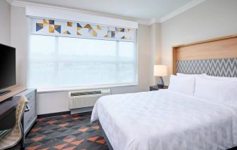 Double bed guest room in Holiday Inn & Suites Oakville At Bronte, with large window and bedside lamp.