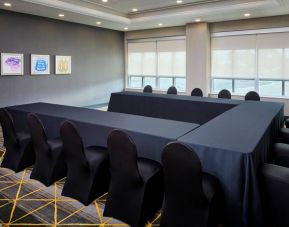 Hotel meeting room with three tables arranged in a U-shape and seating for over a dozen attendees.