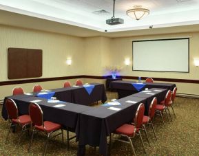 Meeting room with numerous tables, projector screen, and seating for around a dozen.