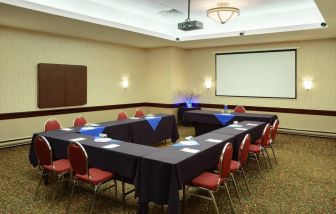 Meeting room with numerous tables, projector screen, and seating for around a dozen.