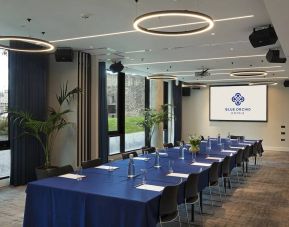 Meeting room with space for over a dozen attendees, featuring large windows and potted plants.
