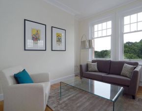 Living room with armchair, sofa, windows, and glass table.