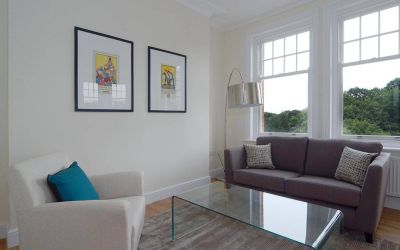 Living room with armchair, sofa, windows, and glass table.