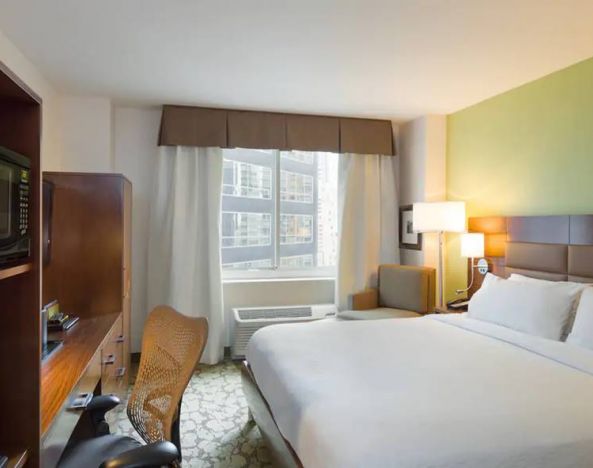 Hilton Garden Inn Midtown East guest room featuring large bed, big windows, and workspace chair and desk.