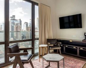 Guest room in The Draper, Ascend Hotel Collection, with two chairs, coffee table, large television, and urban vista through the window.
