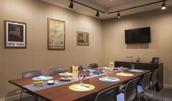 Meeting room with long wooden table, eight chairs, and nearby widescreen TV.