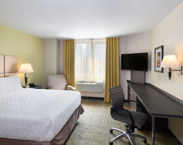 Double bed guest room in the Candlewood Suites Times Square, with workspace nearby and large window.