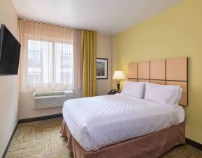 A guest room in the Candlewood Suites Times Square, with double bed, large TV, and window.