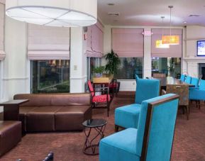 The lounge in the hotel lobby offers comfortable seating on chairs and sofas, with a large TV nearby.