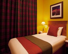 Single bed guest room in The Royal Highland Hotel, with bedside lamp and art on the wall.