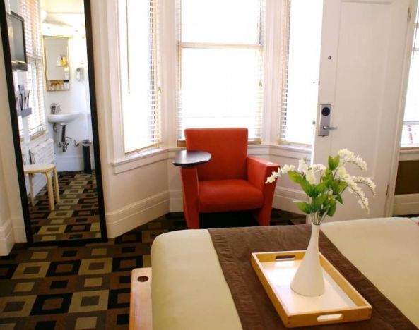 Guest room of The Mosser Hotel, with bed, chair, windows, and ensuite bathroom.