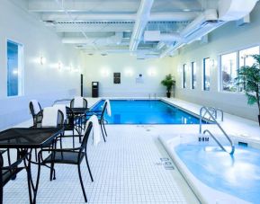 The hotel’s indoor swimming pool has tables, chairs, potted plants, and a hot tub nearby.