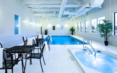 The hotel’s indoor swimming pool has tables, chairs, potted plants, and a hot tub nearby.