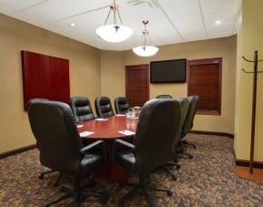 Hotel meeting room with long wooden table, plush leather swivel chairs, and widescreen TV.