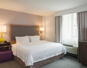 One of the Hampton Inn Times Square South’s king bed guest rooms, with window, TV, and bedside table.