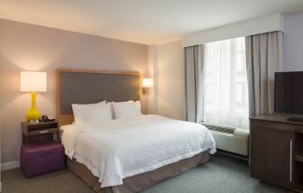 One of the Hampton Inn Times Square South’s king bed guest rooms, with window, TV, and bedside table.