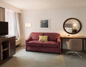 The Hampton Inn Times Square South’s king mobility suite lounge, with desk, sofa, and television.
