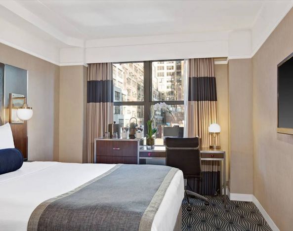 Guest room in the New Yorker Hotel, A Wyndham Hotel, with double bed and workspace desk and chair.