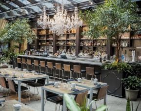 The hotel’s restaurant and bar, with table seating, tall barstools, and plenty of plant life.