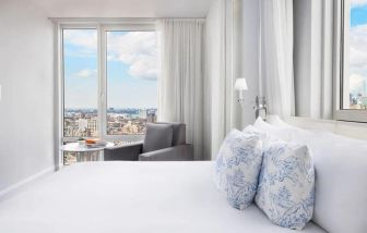 One of the NoMo Soho’s guest rooms, with double bed, chair, and great view of the city.