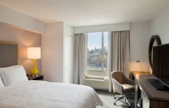 King bedroom with TV, desk, and natural light at Hampton Inn Manhattan Chelsea.