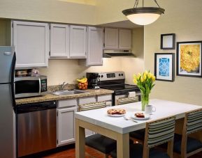 Sonesta ES Suites Tucson guest room kitchen area, equipped with hob, oven, microwave, sink, and fridge freezer, plus dining table.