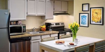 Sonesta ES Suites Tucson guest room kitchen area, equipped with hob, oven, microwave, sink, and fridge freezer, plus dining table.