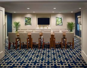 Meeting room in Sonesta ES Suites Tucson, featuring long wooden table, seating for twelve, and a large, wall-mounted television.