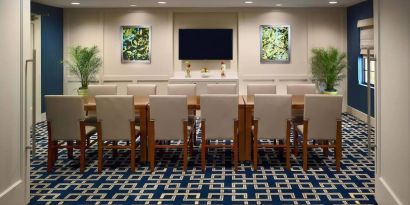 Meeting room in Sonesta ES Suites Tucson, featuring long wooden table, seating for twelve, and a large, wall-mounted television.