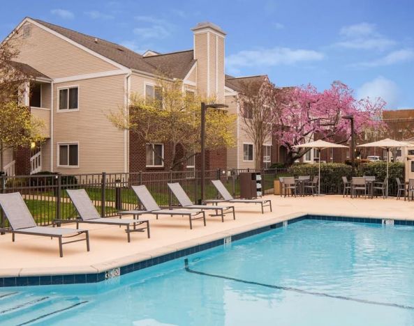 Shaded tables and chairs, as well as sun loungers, are by the side of Sonesta ES Suites Nashville Brentwood’s outdoor pool.