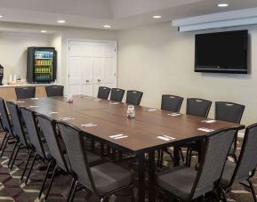 Hotel meeting room, including a long wooden table, projector screen, wall-mounted TV, and seating for over a dozen attendees.