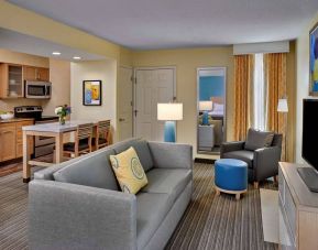Sonesta ES Suites Cincinnati - Blue Ash guest room lounge, with armchair, sofa, and television, plus nearby kitchenette.