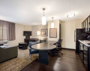 Sonesta Simply Suites Boston Braintree guest room lounge area, furnished with table, chairs, sofa, TV, and adjacent kitchenette.