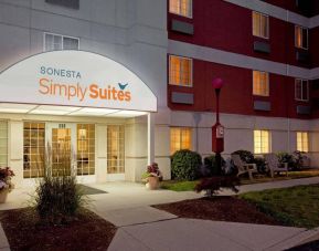 Sonesta Simply Suites Boston Braintree’s exterior has clear signage, potted plants, and chairs on the nearby lawn.